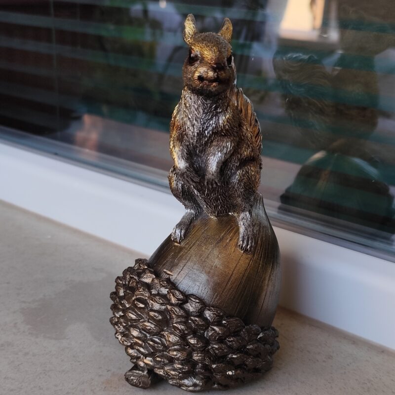 Bronze effect resin squirrel figurine sitting on an acorn, front view