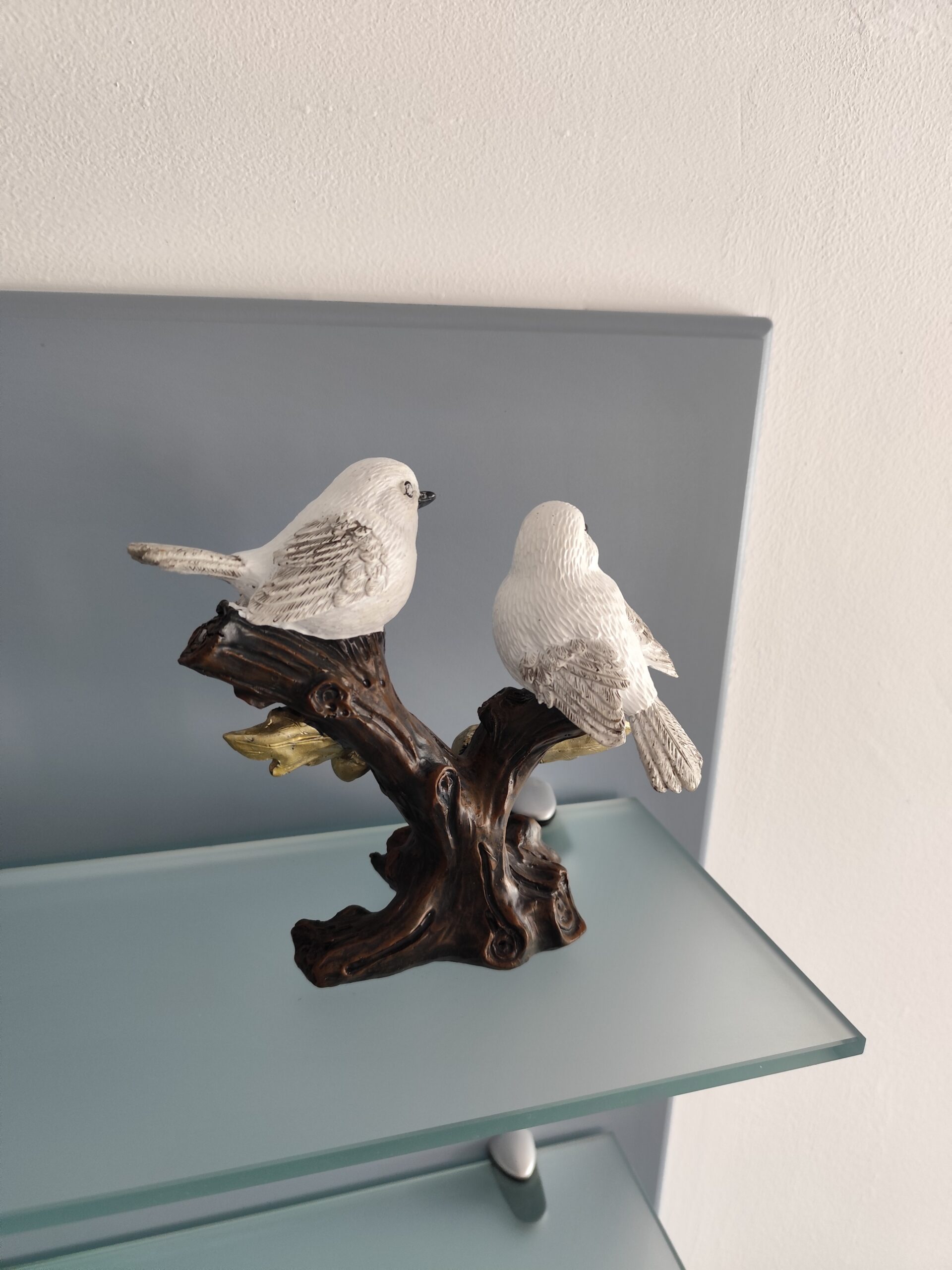 Back view of two white bird figurines on a dark tree branch with golden decorative details