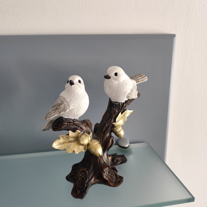 Two white bird resin figurines perched together on a dark decorative branch with golden leaves and acorns