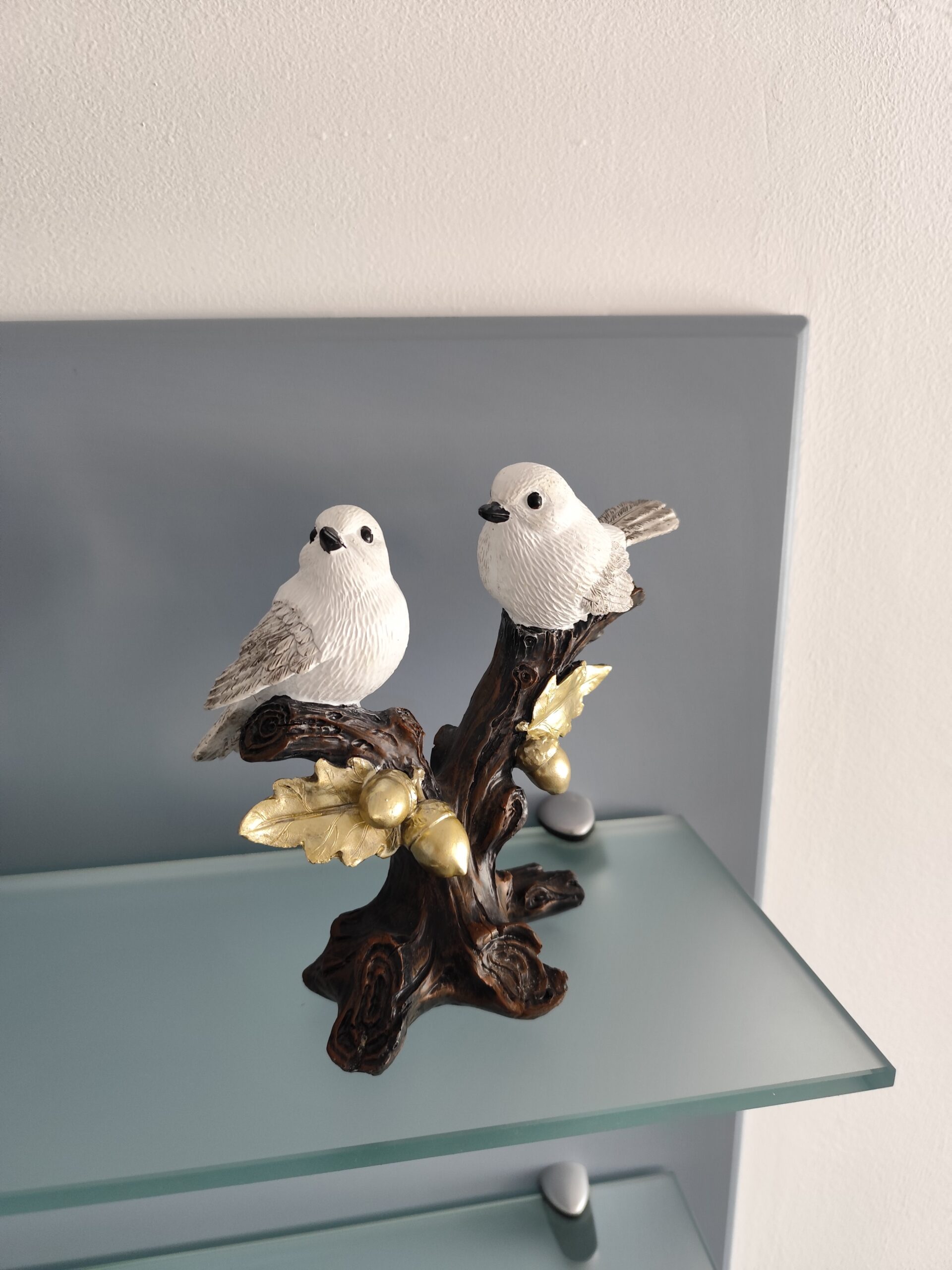 Two white bird resin figurines perched together on a dark decorative branch with golden leaves and acorns