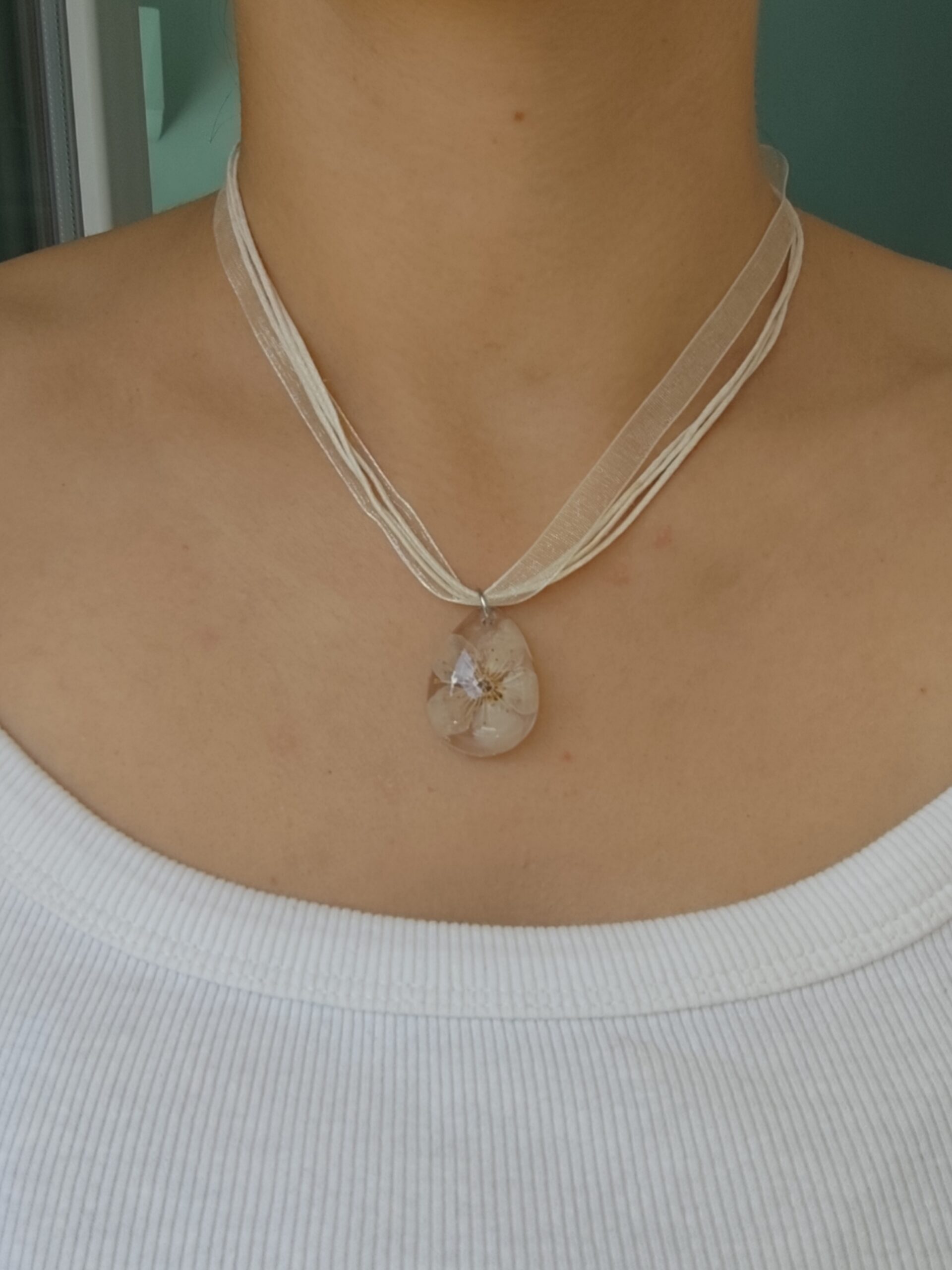 Close-up of a real flower resin pendant necklace with layered white cords