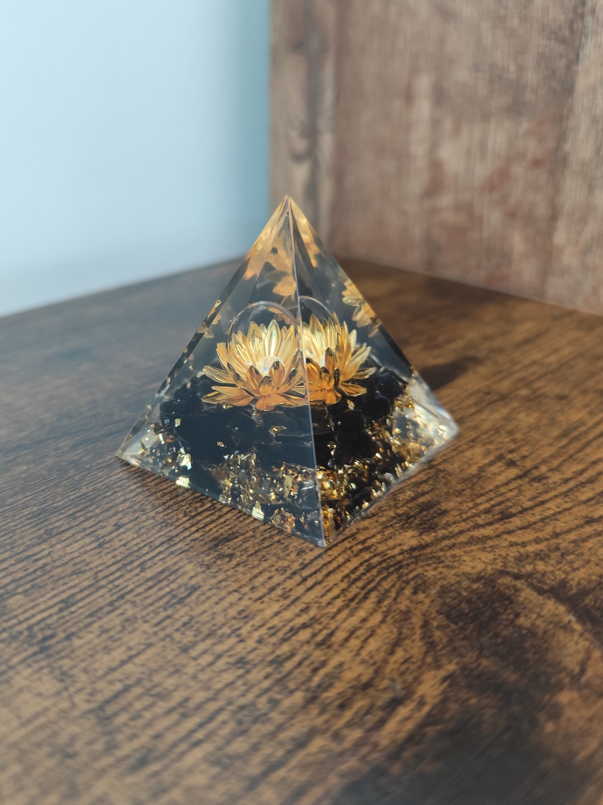 Close-up detail of golden lotus flower and natural obsidian inside a handmade orgonite resin pyramid