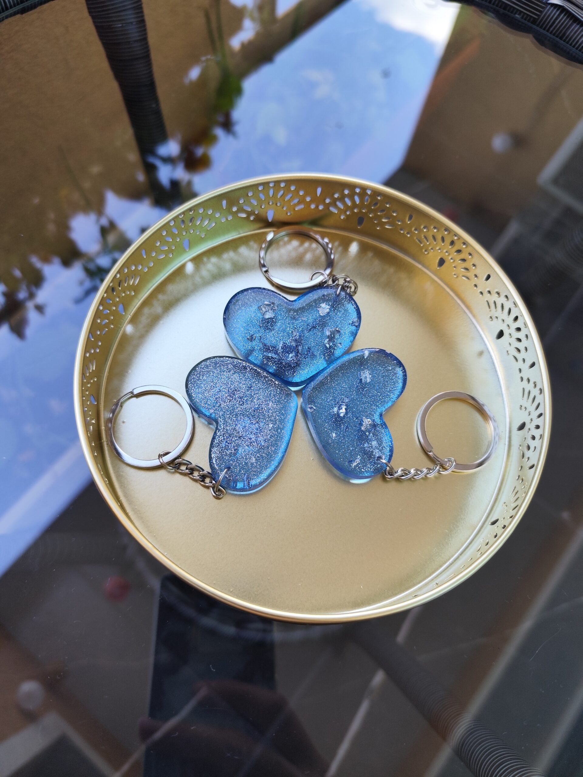 Three handmade blue epoxy resin heart keychains with sparkling finishes and unique decorative details