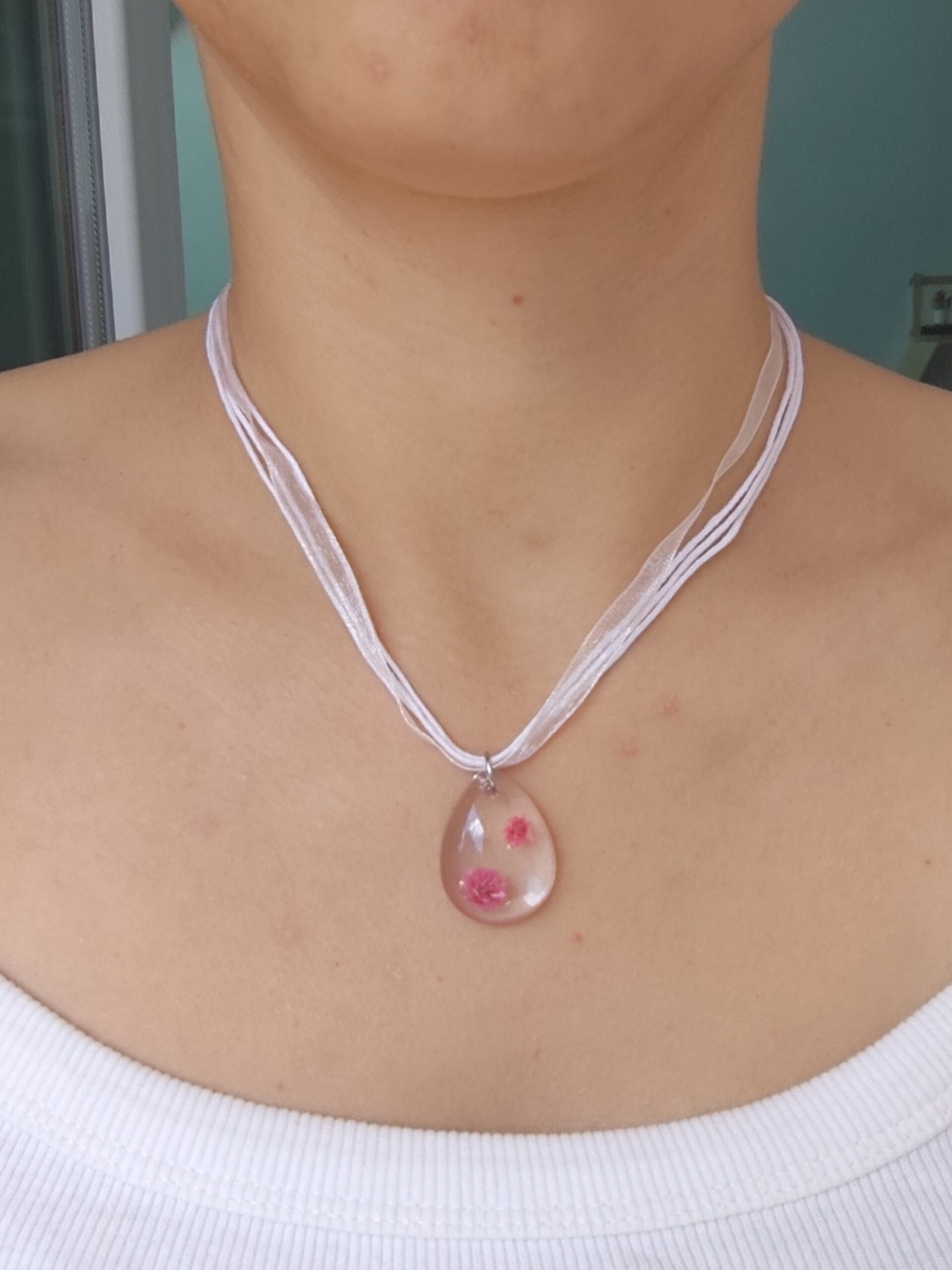 Close-up of a real flower resin pendant necklace with layered white cords